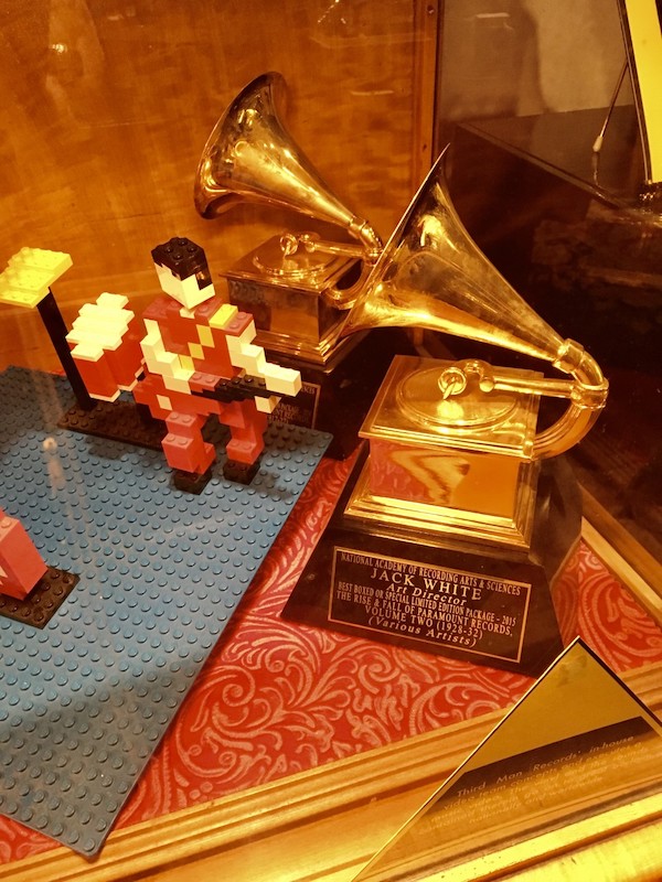 Two of Jack White's Grammy in a showcase on top of some red and gold fabric with a LEGO figure made out of blocks next to them at Third Man Records in Nashville, TN.